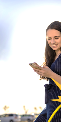 Woman watching at her smartphone near a EV charging station